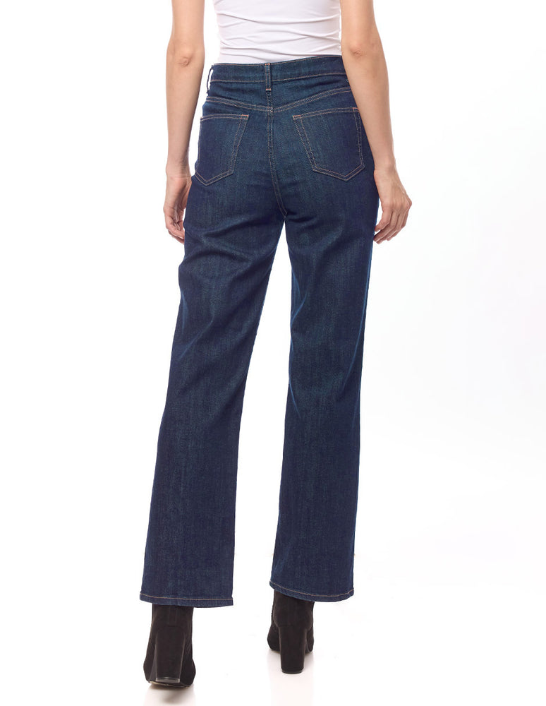 
                  
                    Mujer con jeans denim recto azul, vista trasera, combinados con una camiseta blanca y tacones negros.
                  
                